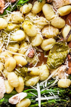 Top down shot of a section of sheet pan gnocchi showing baked gnocchi, chicken, broccolini topped with parmesan cheese and a spoon of pesto.