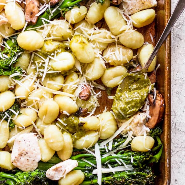Top down shot of a section of sheet pan gnocchi showing baked gnocchi, chicken, broccolini topped with parmesan cheese and a spoon of pesto.