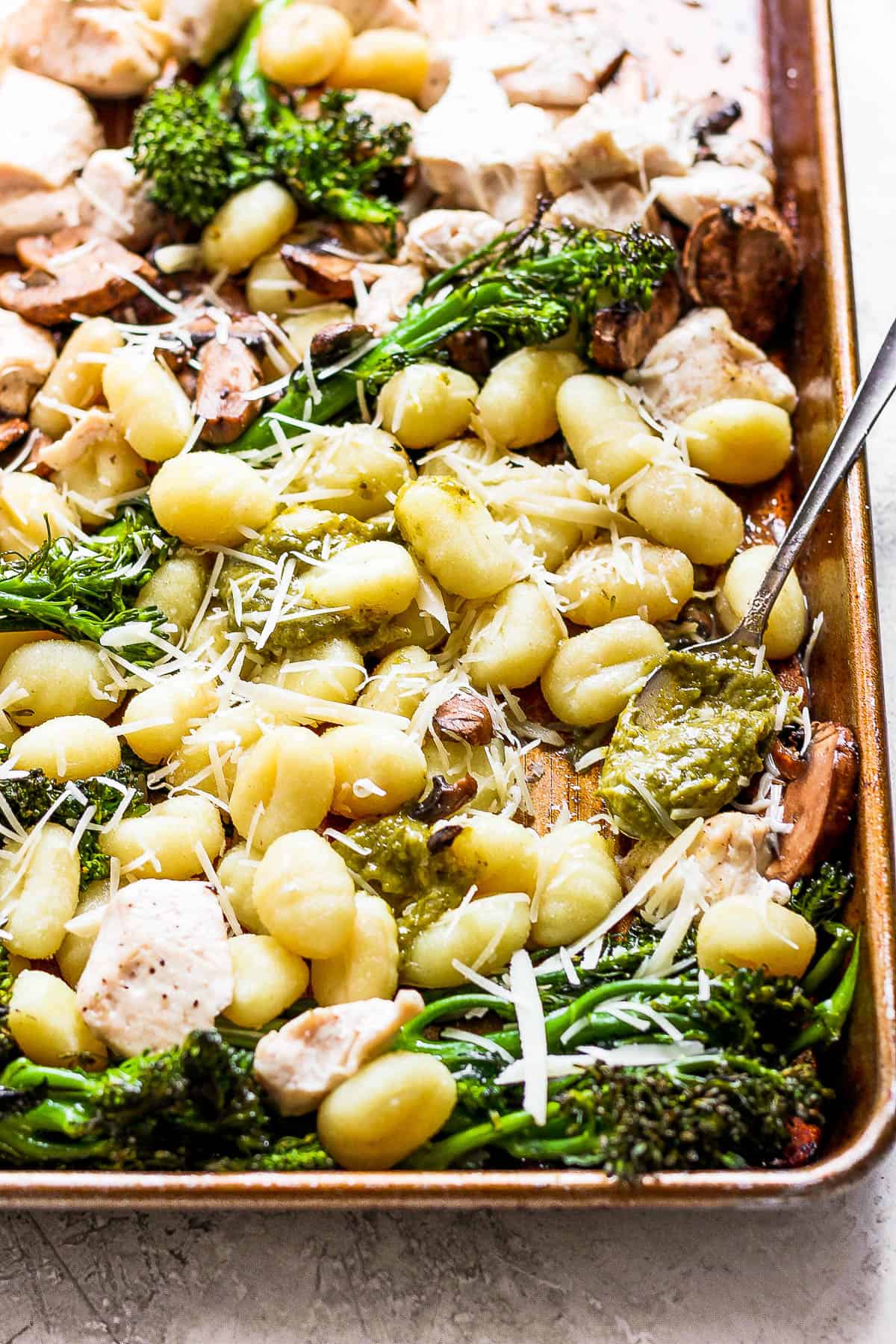 Sheet pan chicken and gnocchi on a baking sheet with peso and fresh parmesan cheese.