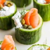 Side shot of a smoked salmon appetizer in a cucumber cup with salmon, dill sauce, capers and dill.
