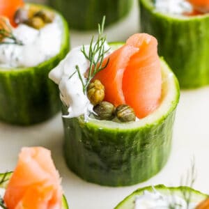 Side shot of a smoked salmon appetizer in a cucumber cup with salmon, dill sauce, capers and dill.