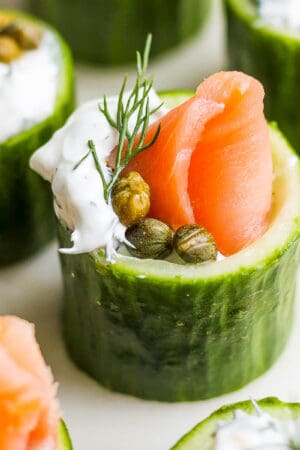 Side shot of a smoked salmon appetizer in a cucumber cup with salmon, dill sauce, capers and dill.