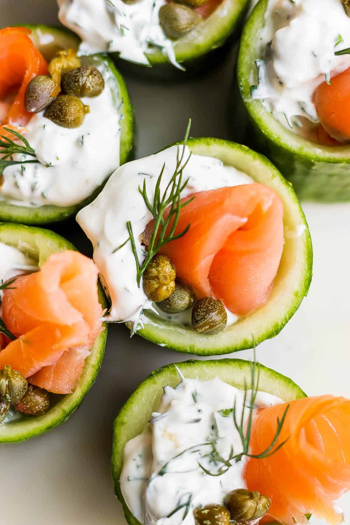 Five cucumber cups filled with dill sauce, three capers, smoked salmon, and a tiny sprig of fresh dill.