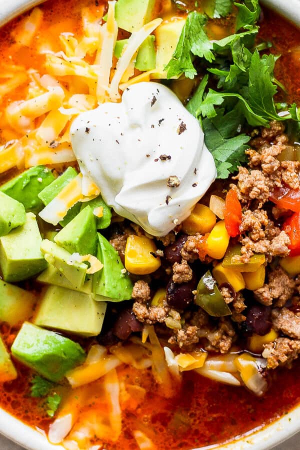 Top down shot of a bowl of taco soup with avocado, cilantro, cheese and sour cream on top.