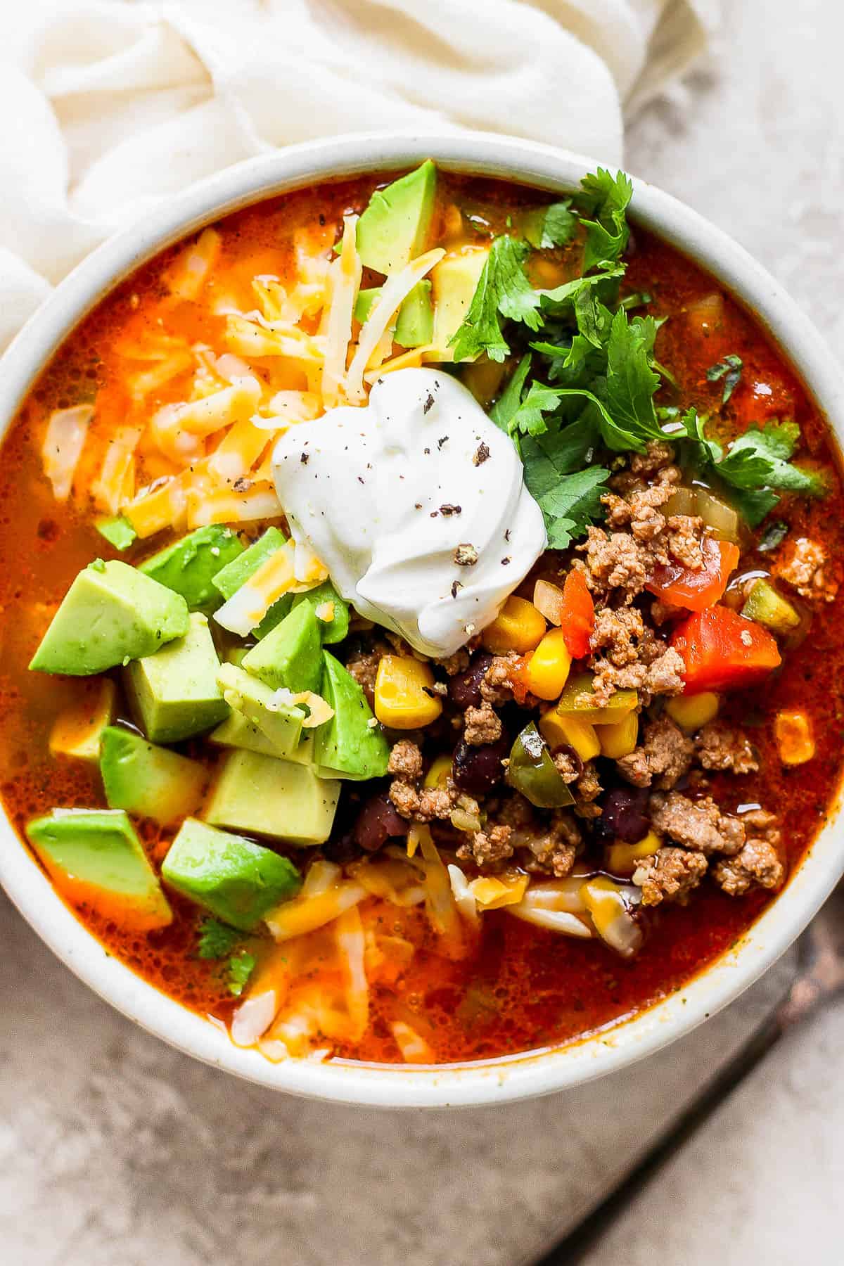 Taco soup in a bowl topped with shredded cheese, cilantro, sour cream, and avocado.