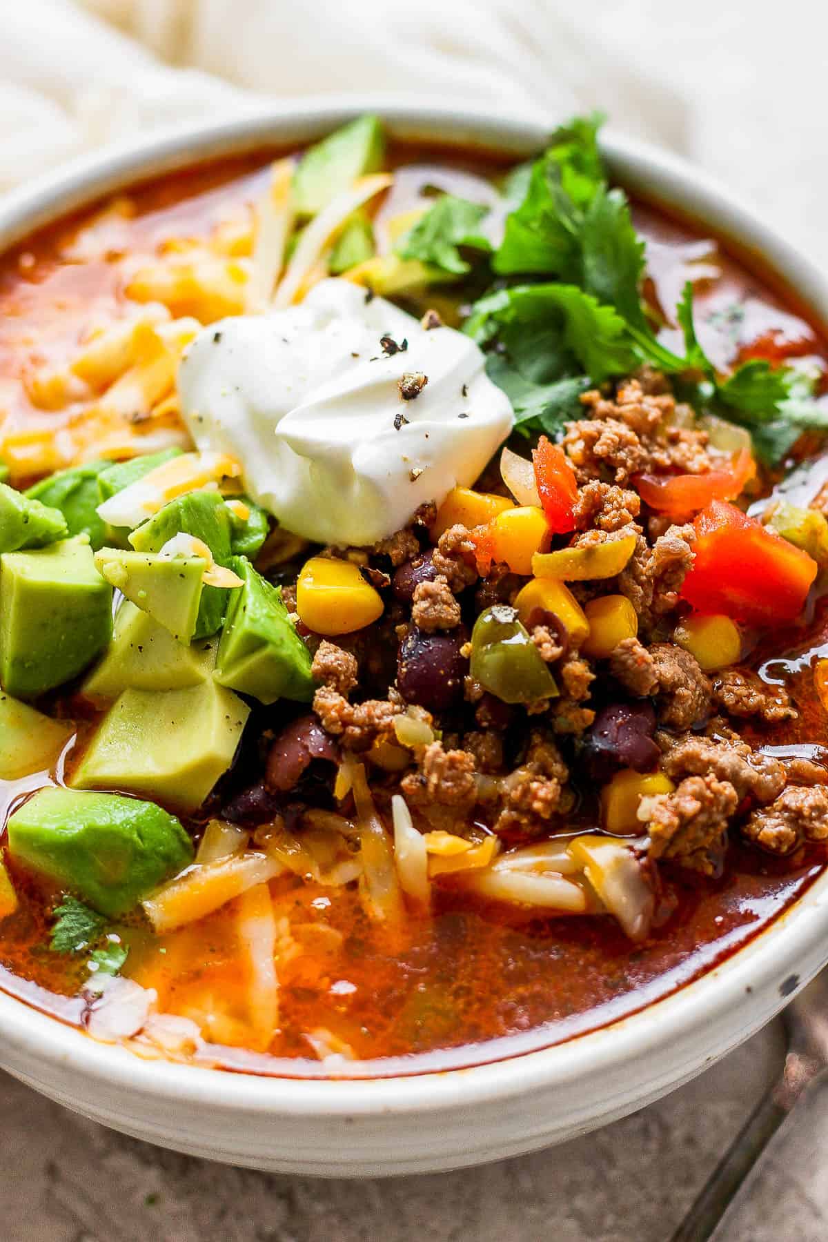 Taco soup in a bowl topped with shredded cheese, cilantro, sour cream, and avocado.