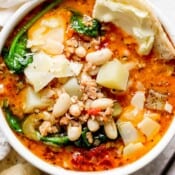 Top down shot of a bowl of tuscan white bean soup with spinach and shaved parmesan cheese on top.