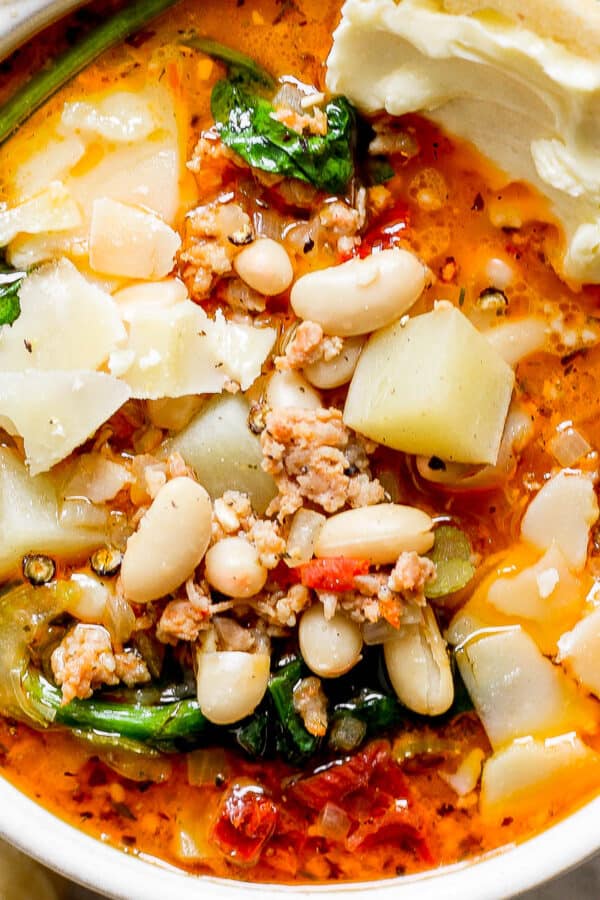 Top down shot of a bowl of tuscan white bean soup with spinach and shaved parmesan cheese on top.