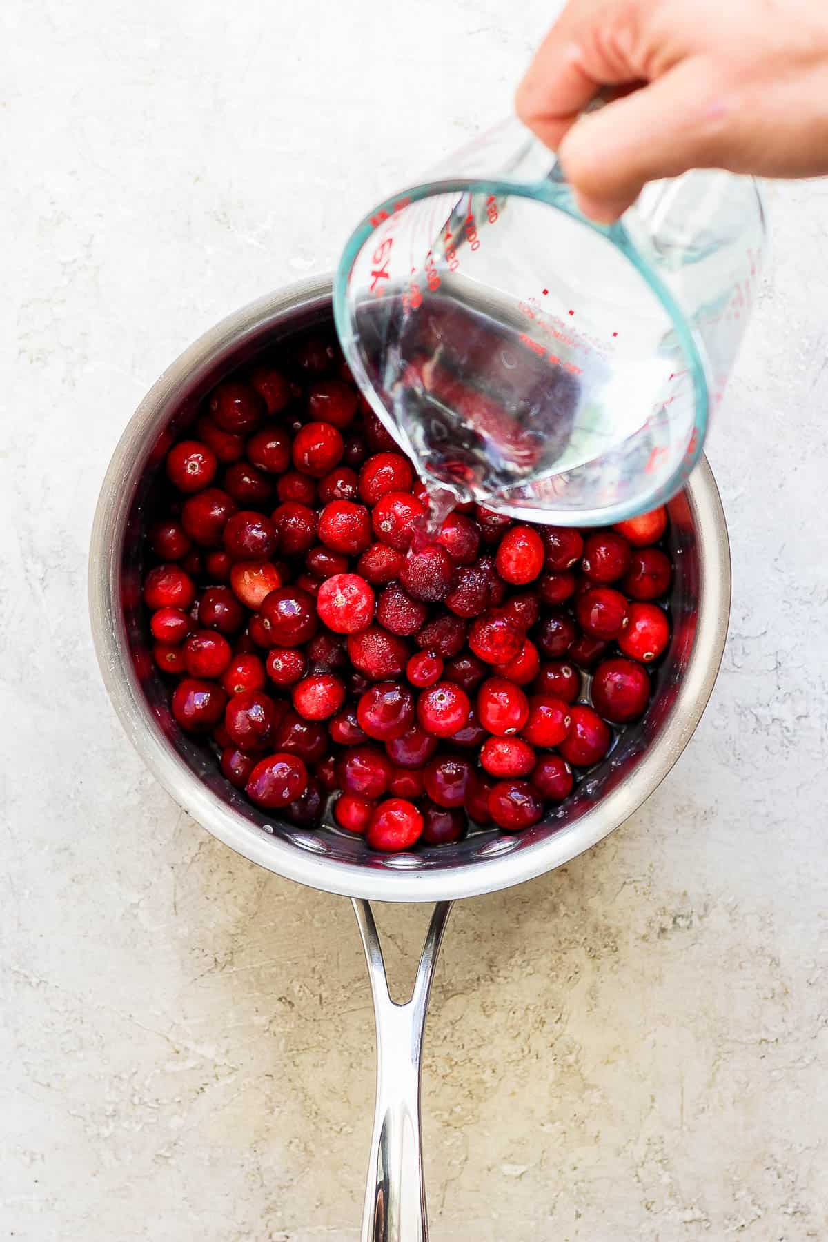 Water being poured into a sauce pan with cranberries.