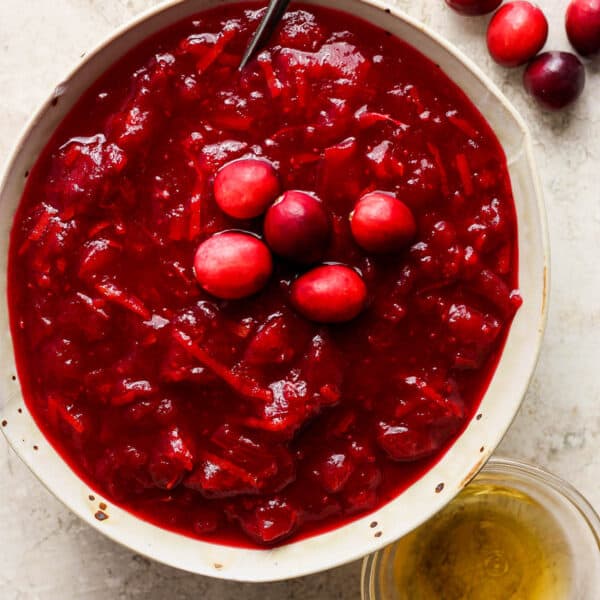 Top down shot of a bowl of bourbon cranberry sauce with a spoon sticking out and five raw cranberries as a garnish on top.