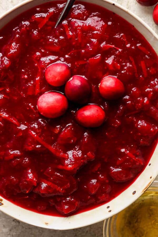 Top down shot of a bowl of bourbon cranberry sauce with a spoon sticking out and five raw cranberries as a garnish on top.
