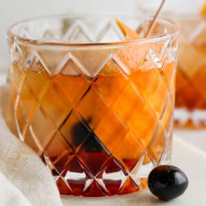 Lowball glass filled with a brandy old fashioned with an orange peel and cherry garnish.