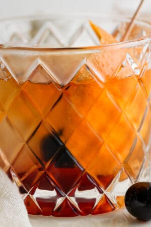 Lowball glass filled with a brandy old fashioned with an orange peel and cherry garnish.