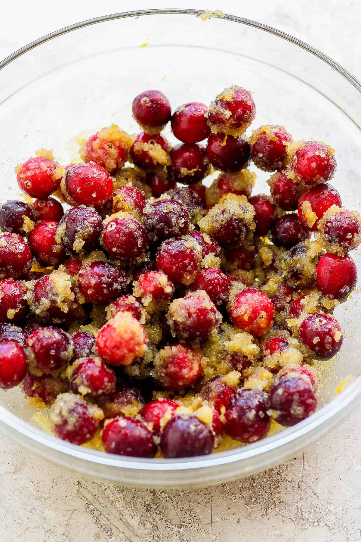 A medium bowl with cranberries coated in the cornstarch, cane sugar, orange zest, orange juice and vanilla extract mixture. 