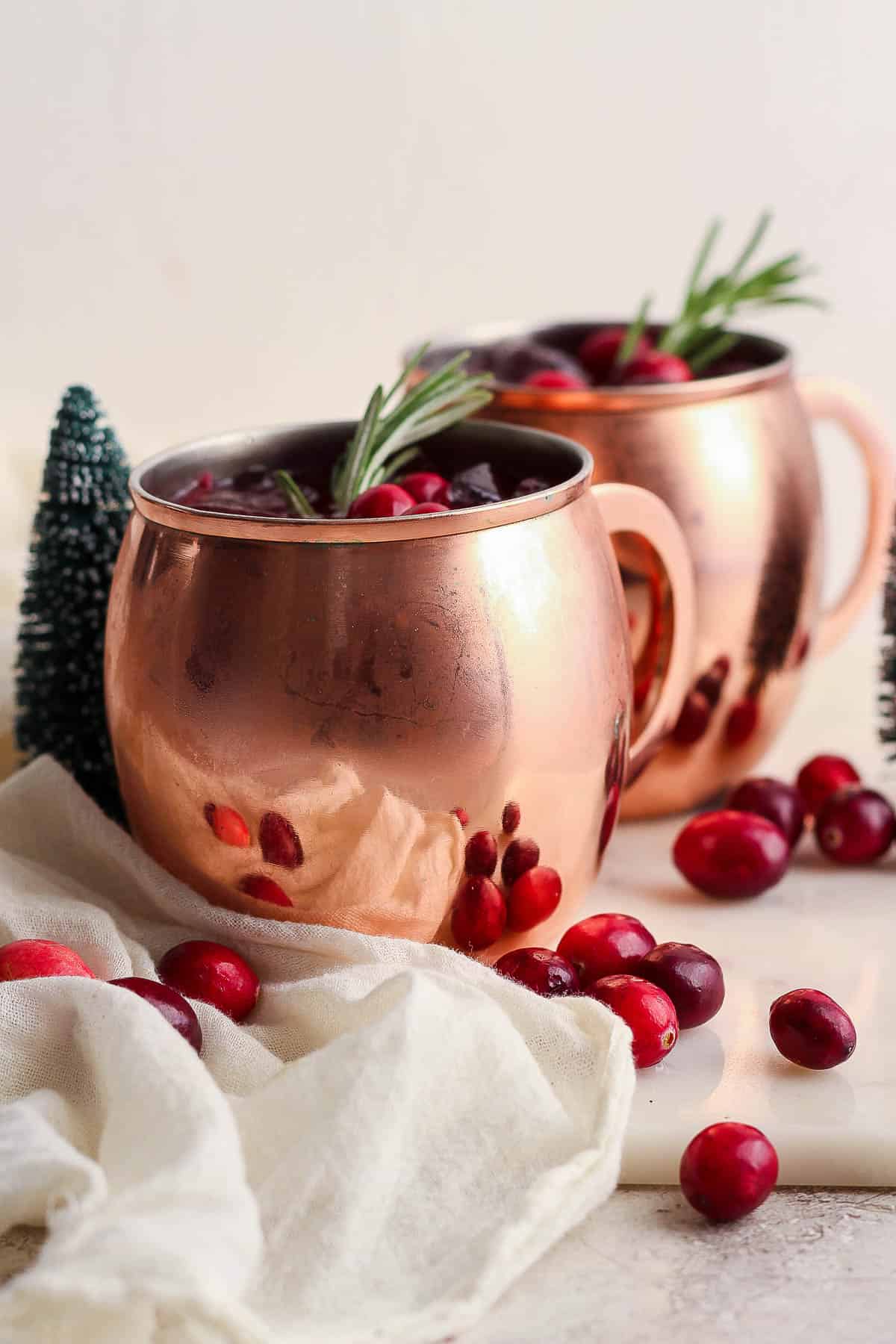Two cranberry moscow mule cocktails in copper mugs.