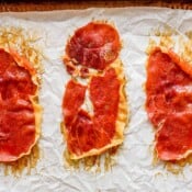 Top down shot of three pieces of crispy prosciutto on a parchment lined baking sheet.