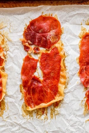 Top down shot of three pieces of crispy prosciutto on a parchment lined baking sheet.