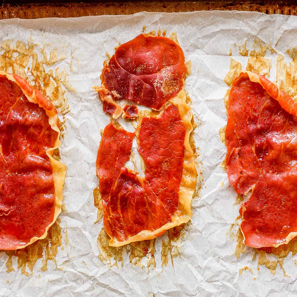 Top down shot of three pieces of crispy prosciutto on a parchment lined baking sheet.