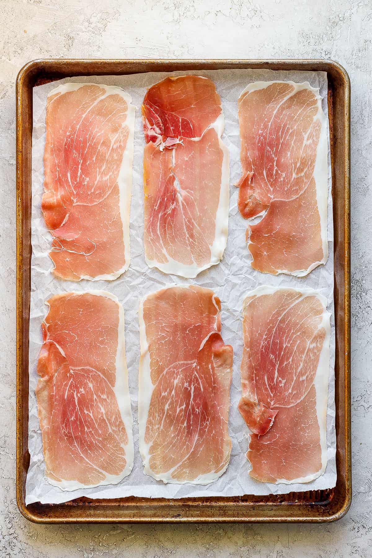 Slices of prosciutto on a parchment-lined baking sheet.