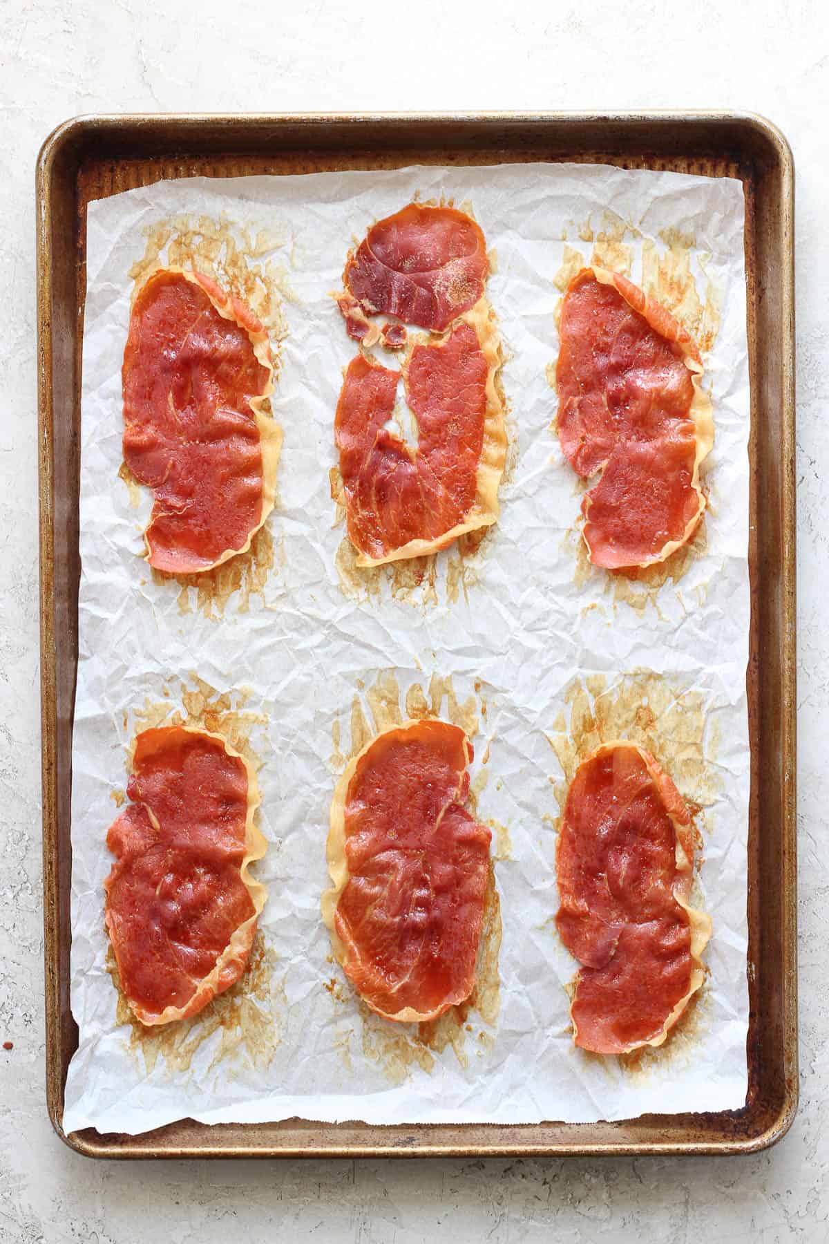 Crispy prosciutto on a baking sheet after being cooked.