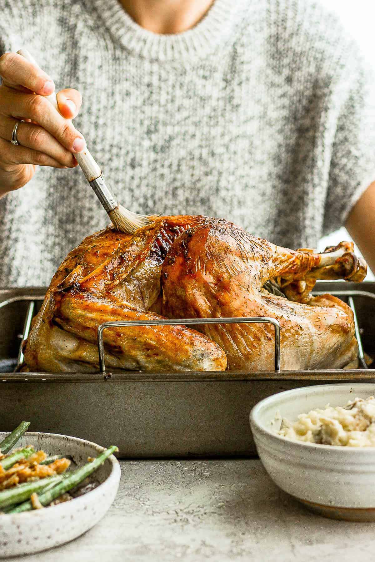 A fully cooked turkey being basted with melted butter.