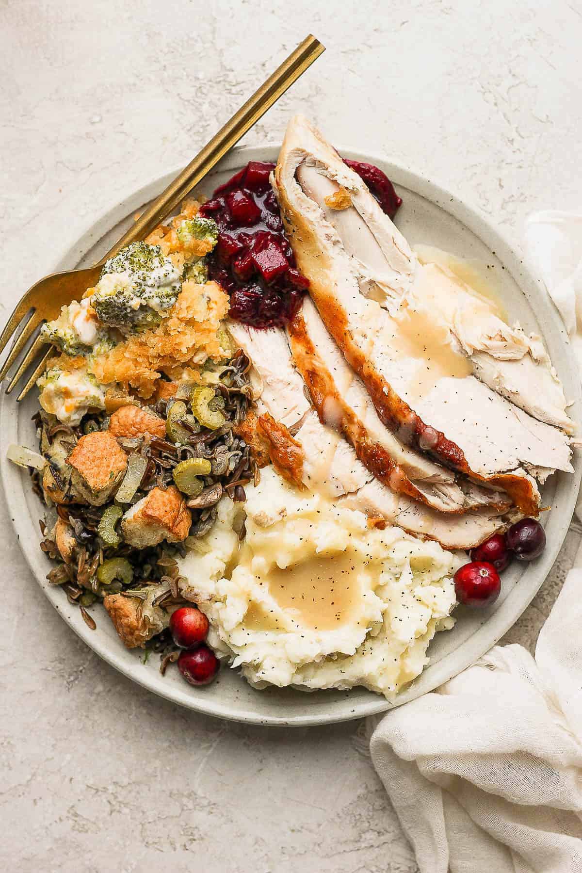 Turkey slices on a plate with stuffing, broccoli casserole, and cranberry sauce.
