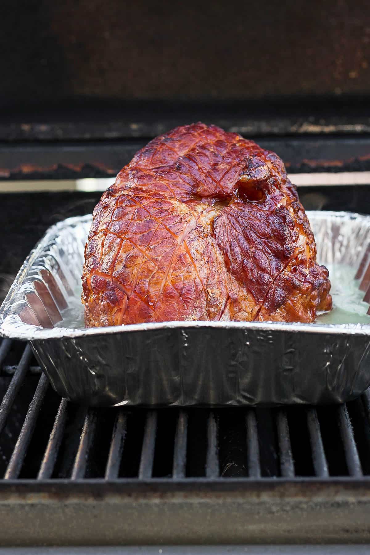 The ham in the roasting pan and being placed on the grill.