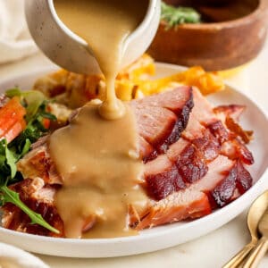 A plate of sliced ham with ham gravy being poured on top.