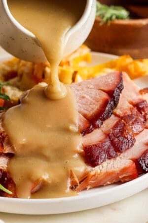 A plate of sliced ham with ham gravy being poured on top.