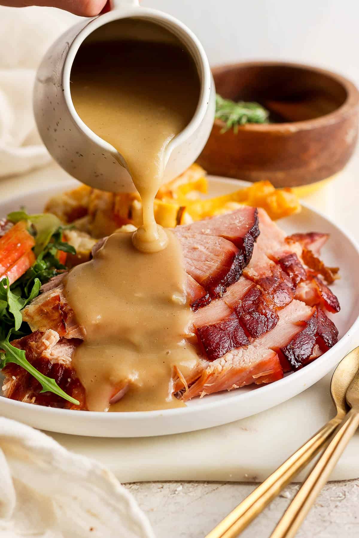 A white plate with ham slices and sides with ham gravy being poured on top.