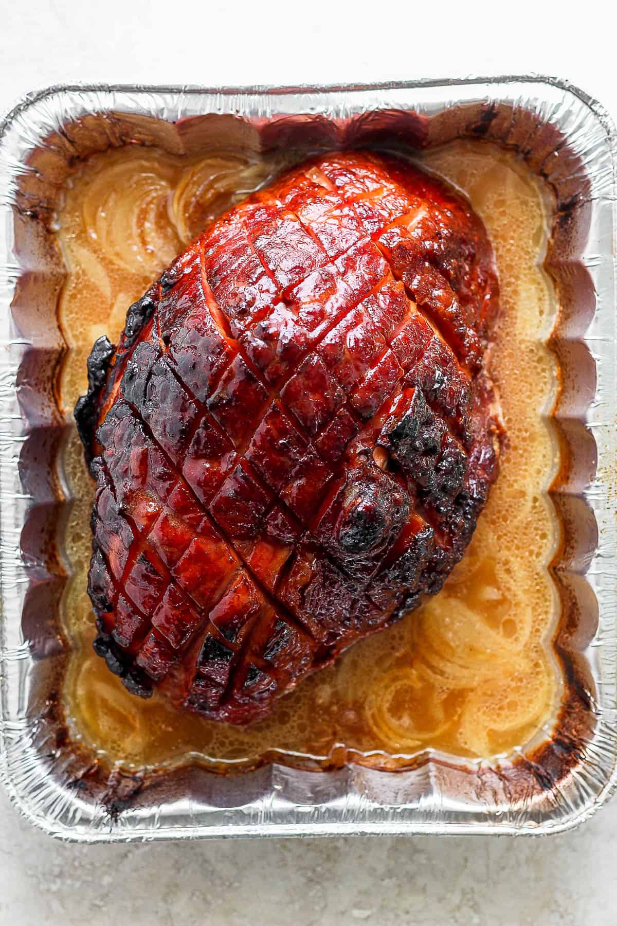A fully cooked ham in an aluminum roasting pan.