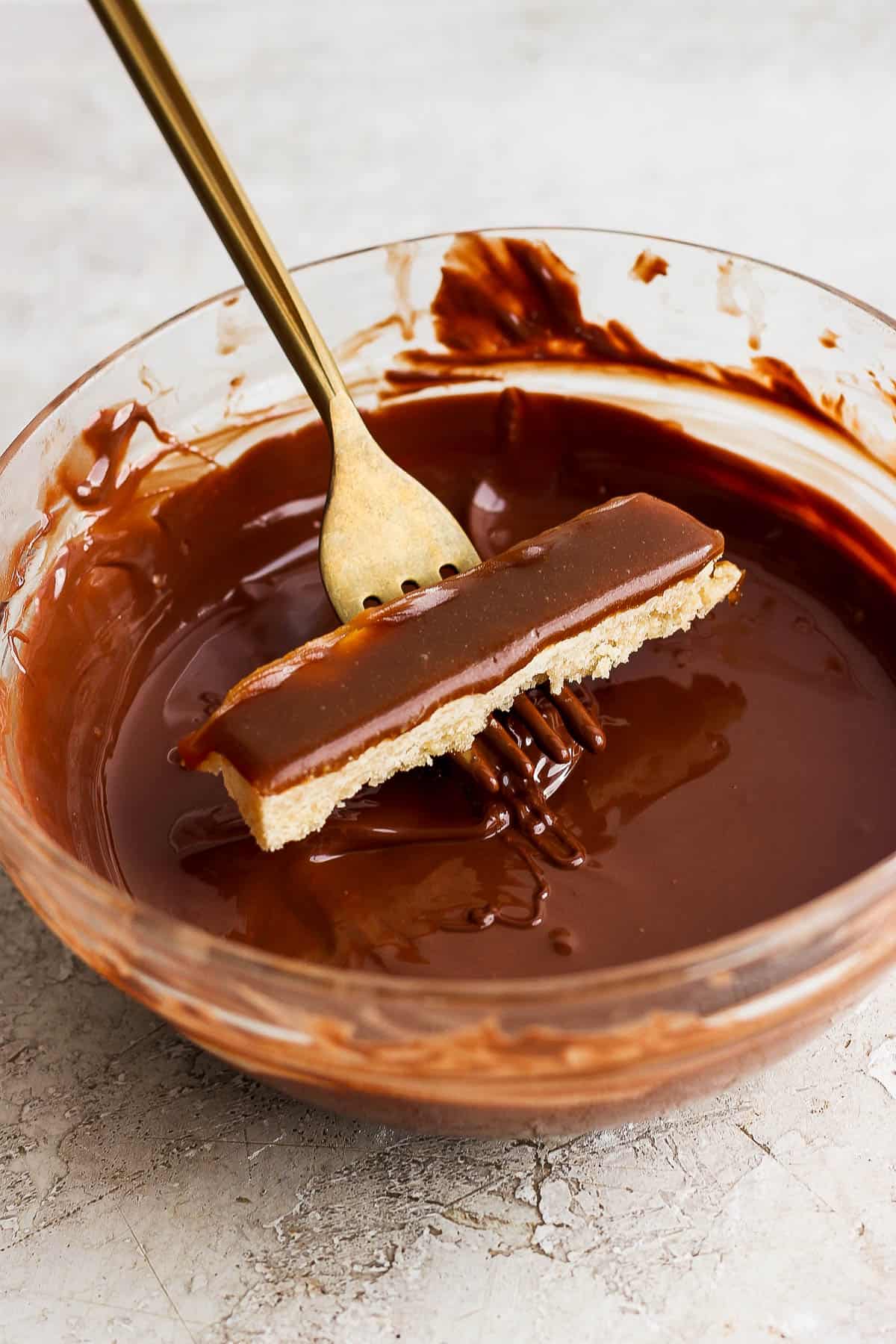 A fork holding a twix bar over the bowl of melted chocolate.