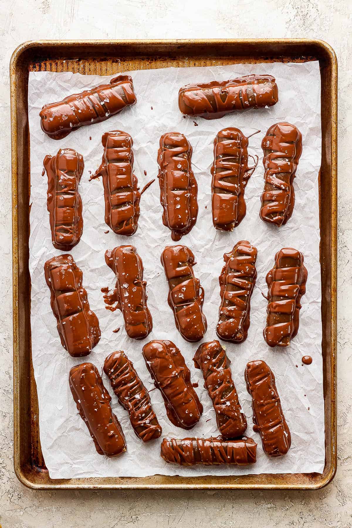 All of the twix bars coated in chocolate and placed on a parchment-lined baking sheet.