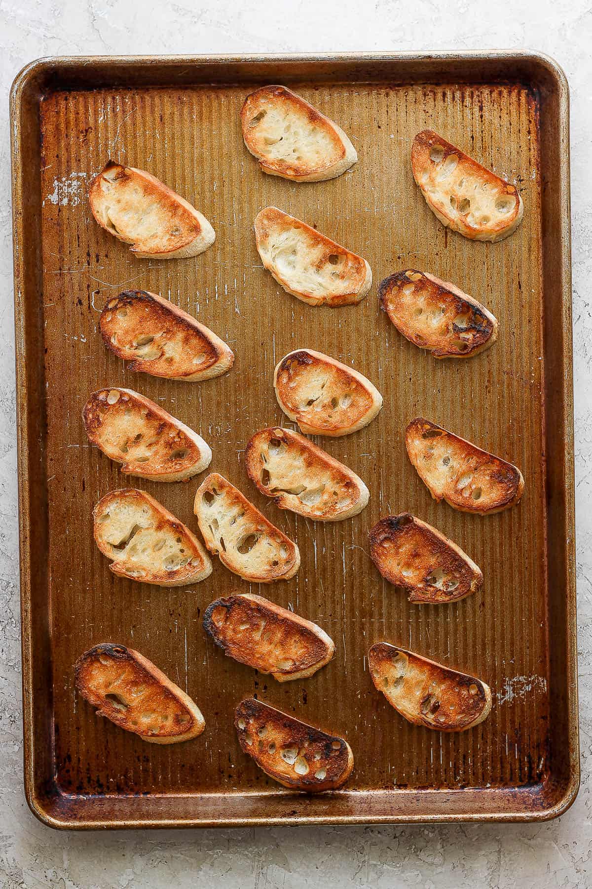 Toasted pieces of crostini on a baking sheet.