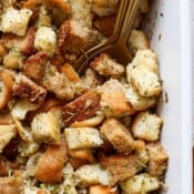 Top down close up shot of a golden spoon sticking out of a baking dish filled with a homemade stuffing recipe.