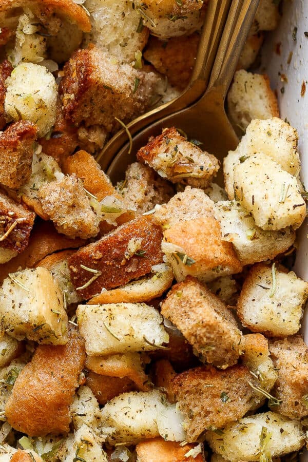 Top down close up shot of a golden spoon sticking out of a baking dish filled with a homemade stuffing recipe.