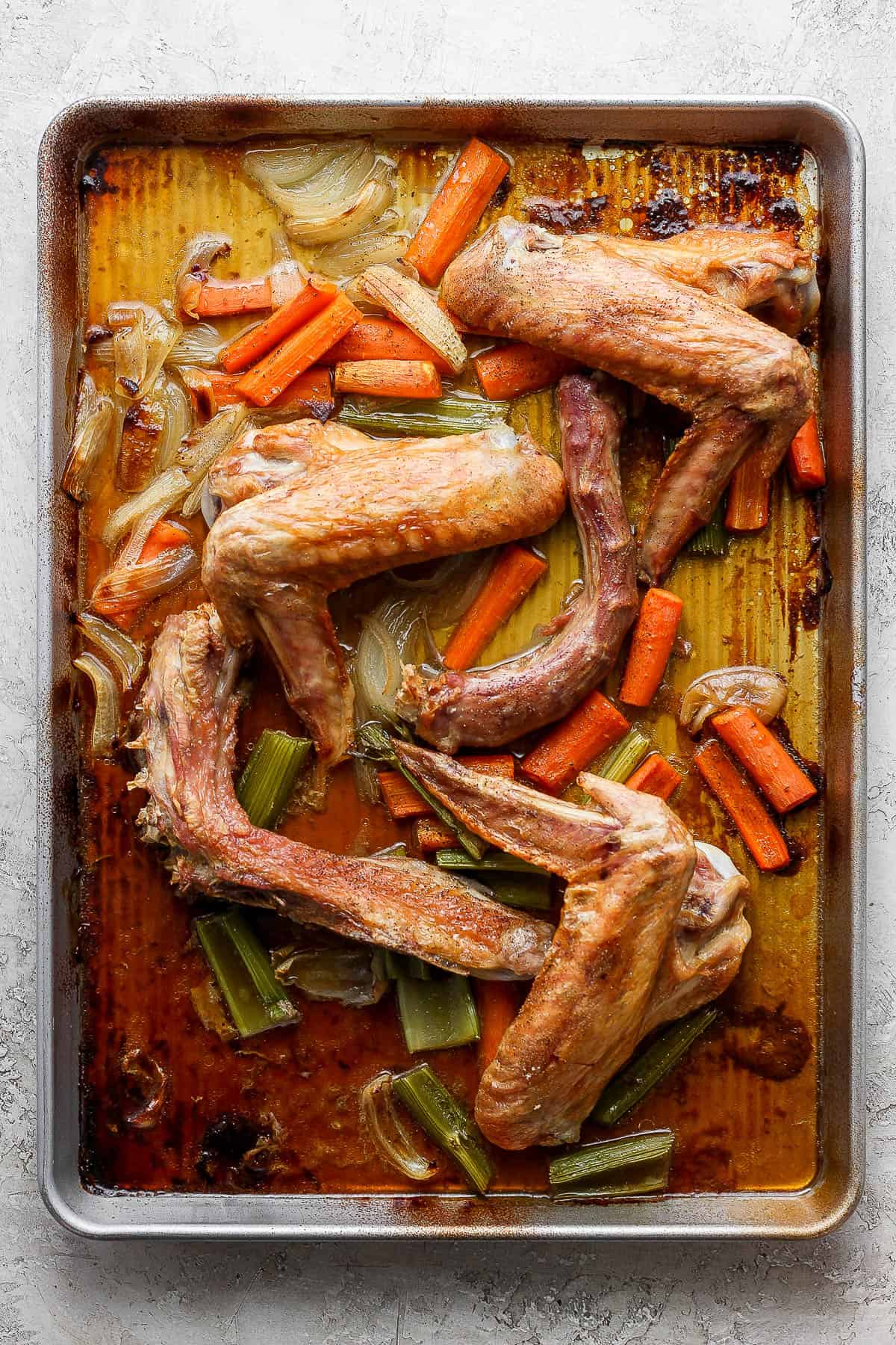 Roasted turkey legs, carrots, celery, and onion on a baking sheet.