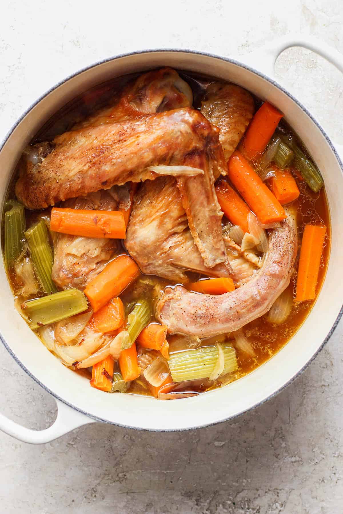 Turkey parts, roasted veggies, and turkey stock in a dutch oven.