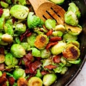 Top down shot of a cast iron skillet filled with maple bacon brussel sprouts and a wooden spoon sticking out.