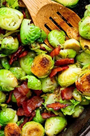 Top down shot of a cast iron skillet filled with maple bacon brussel sprouts and a wooden spoon sticking out.