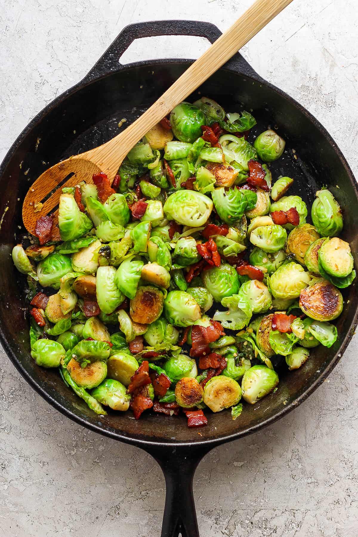 Maple bacon brussels sprouts in a skillet with a wooden spoon.