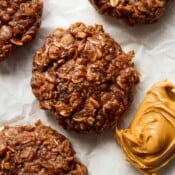 Top down shot of a 4 no bake cookies on a piece of parchment paper with a spoon of creamy peanut butter next to them.