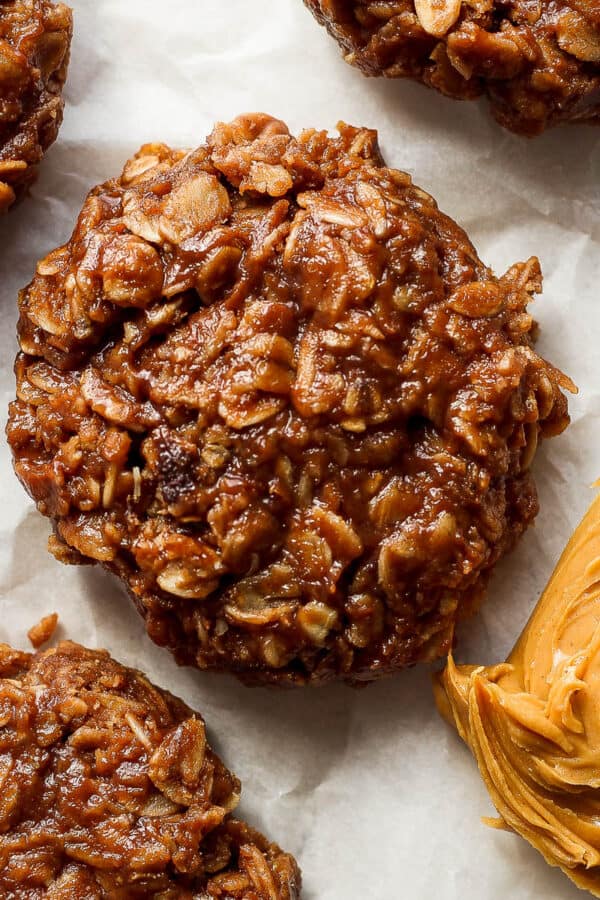 Top down shot of a 4 no bake cookies on a piece of parchment paper with a spoon of creamy peanut butter next to them.
