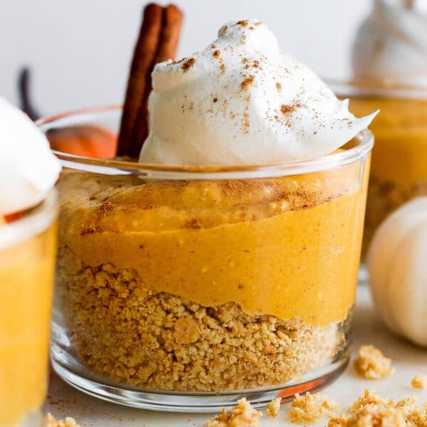 A short glass filled with graham cracker crust, pumpkin pie filling and whipped cream to make pumpkin pie in a cup.