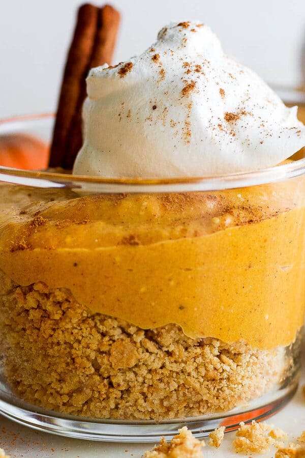 A short glass filled with graham cracker crust, pumpkin pie filling and whipped cream to make pumpkin pie in a cup.