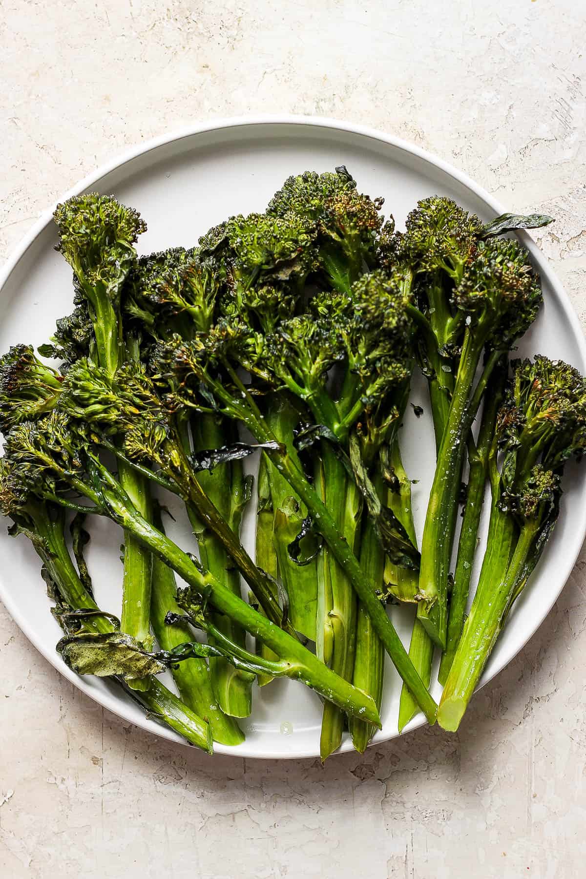 Roasted broccolini spears on a white plate.