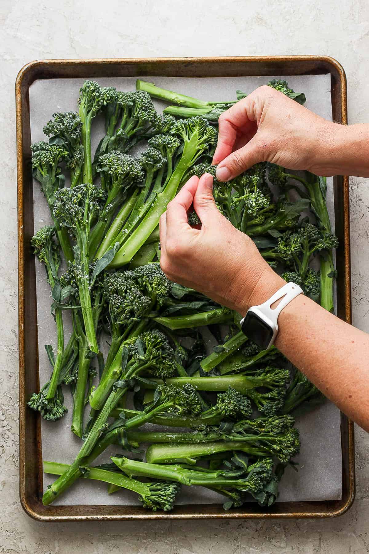 Two hands massaging the olive oil on each piece of broccolini.