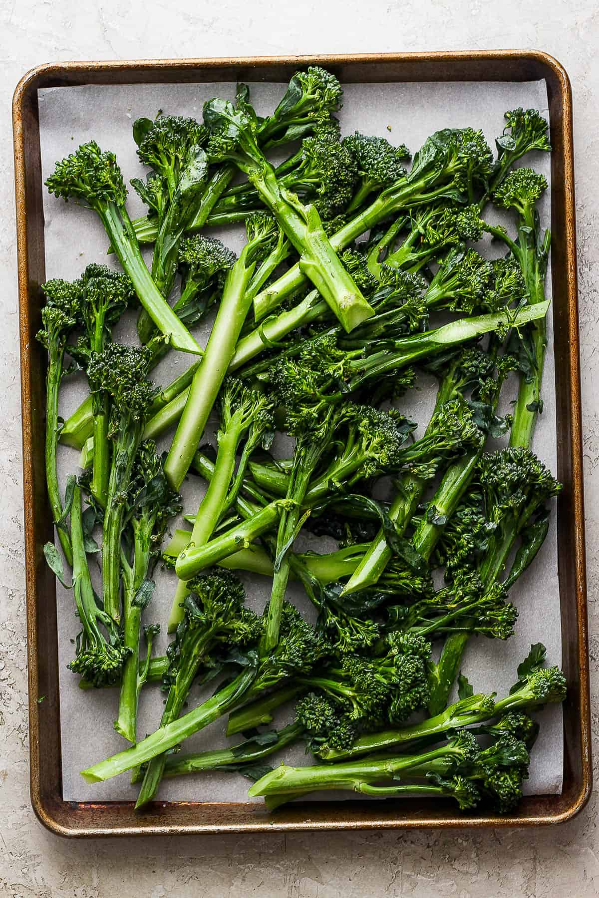 Oiled and seasoned broccolini on a baking sheet before baking.
