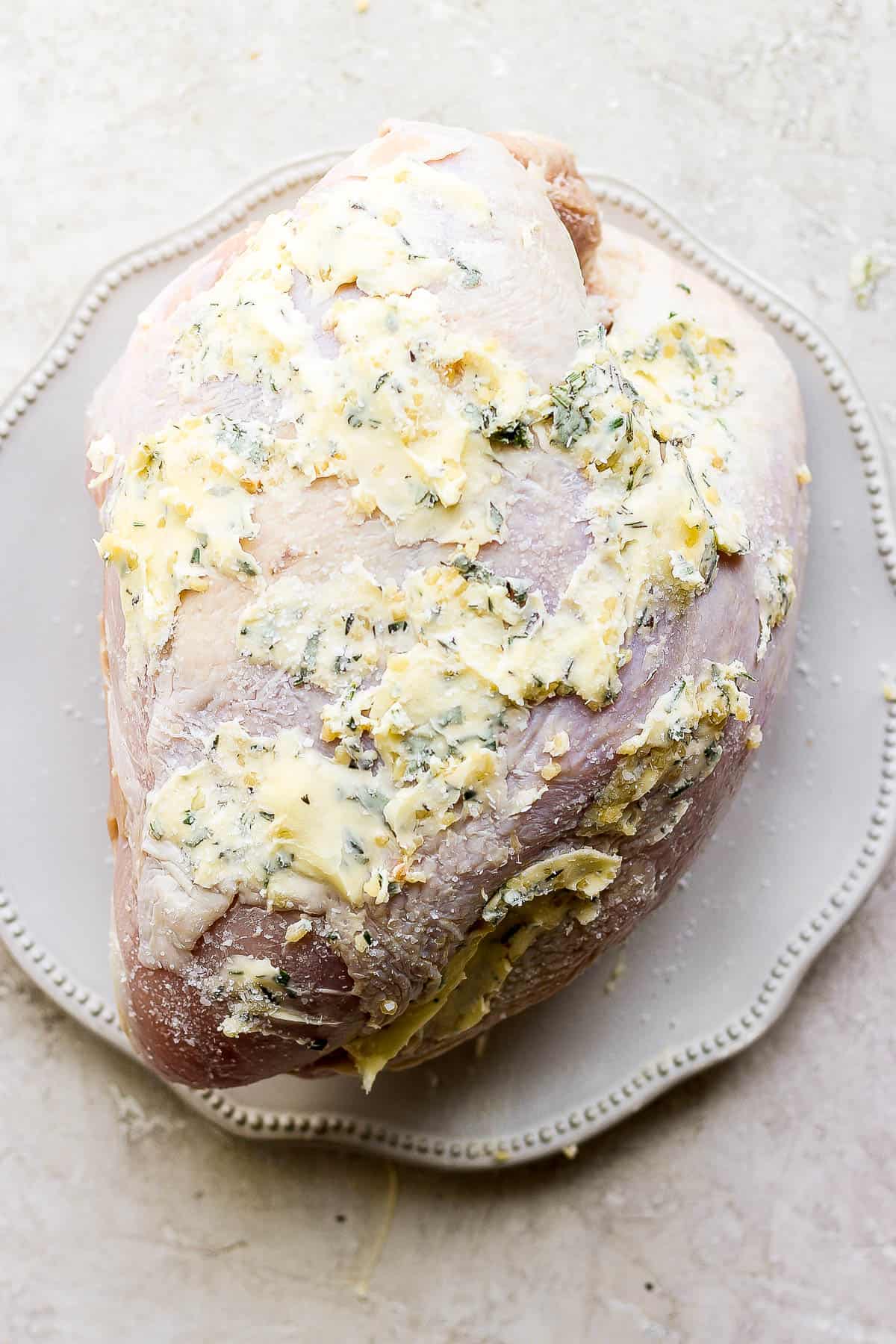 Turkey breast on a plate covered in the herbed butter, salt, and pepper.