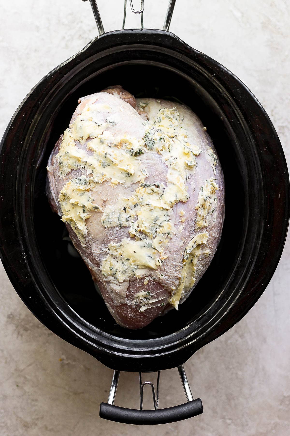 Buttered turkey breast placed in the slow cooker on top of the onions, herbs, etc.